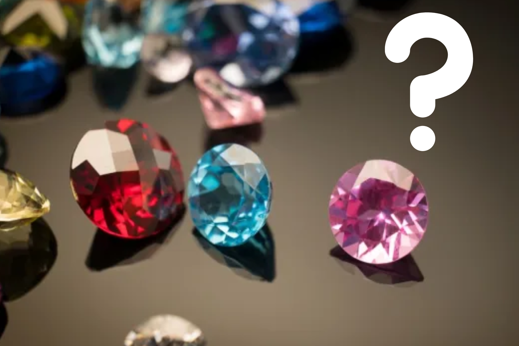 A group of colorful birthstones is arranged beside a large white question mark symbol