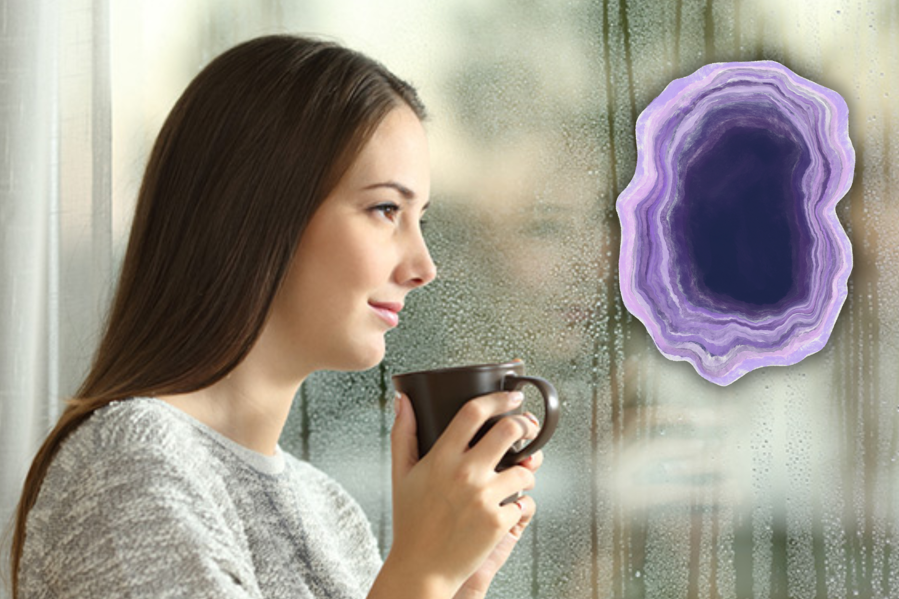 A view of a woman sitting in front of a window, holding a cup of coffee and with an amethyst stone nearby.