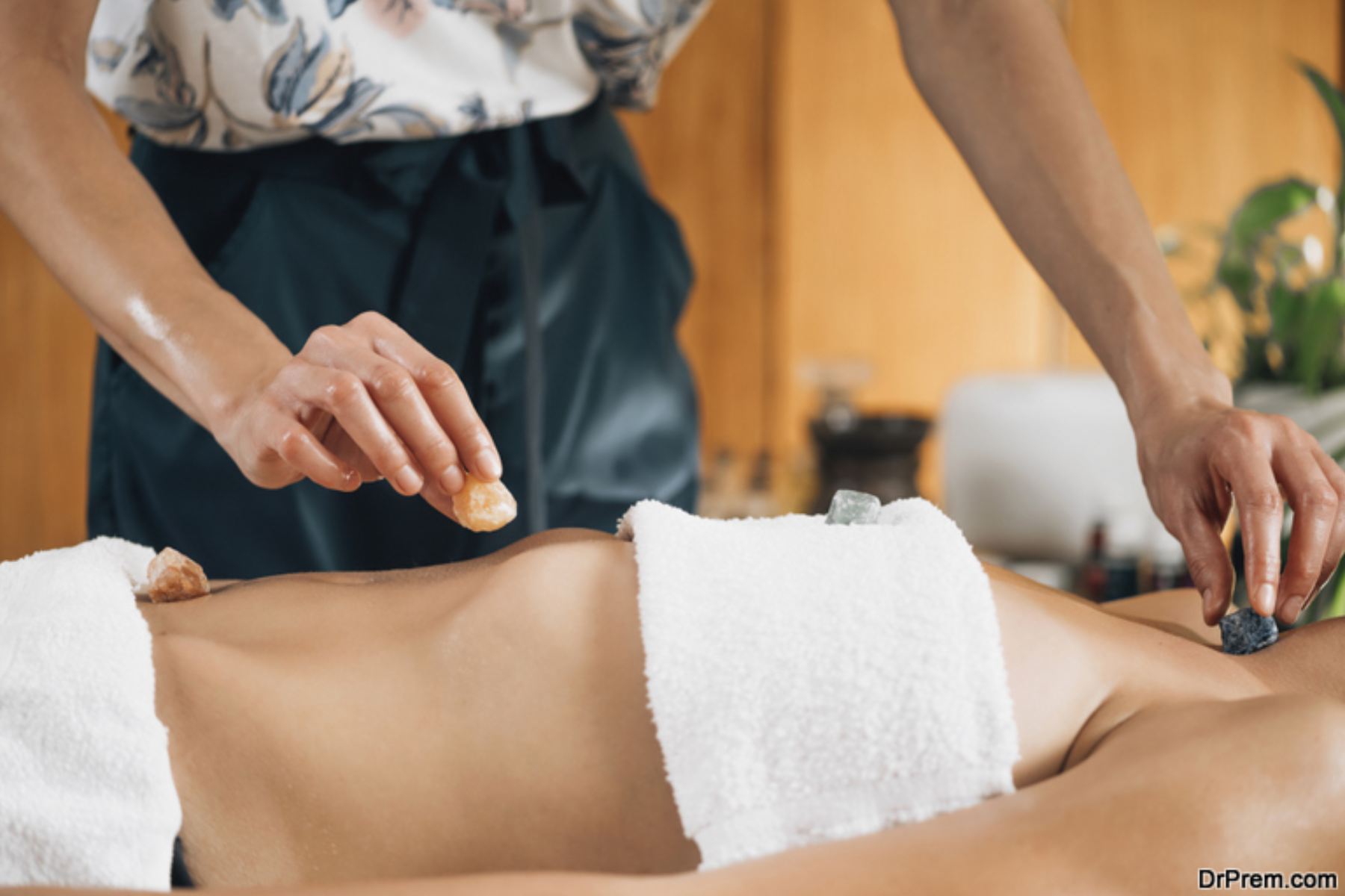 A bodywork therapist placing gemstones on a female client's abdomen and neck during a therapy session