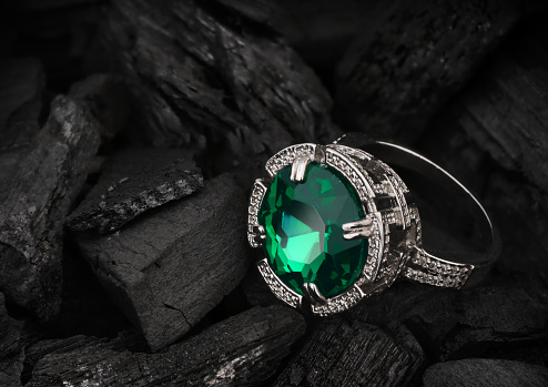 Jewelry ring with big green emerald on dark coal background
