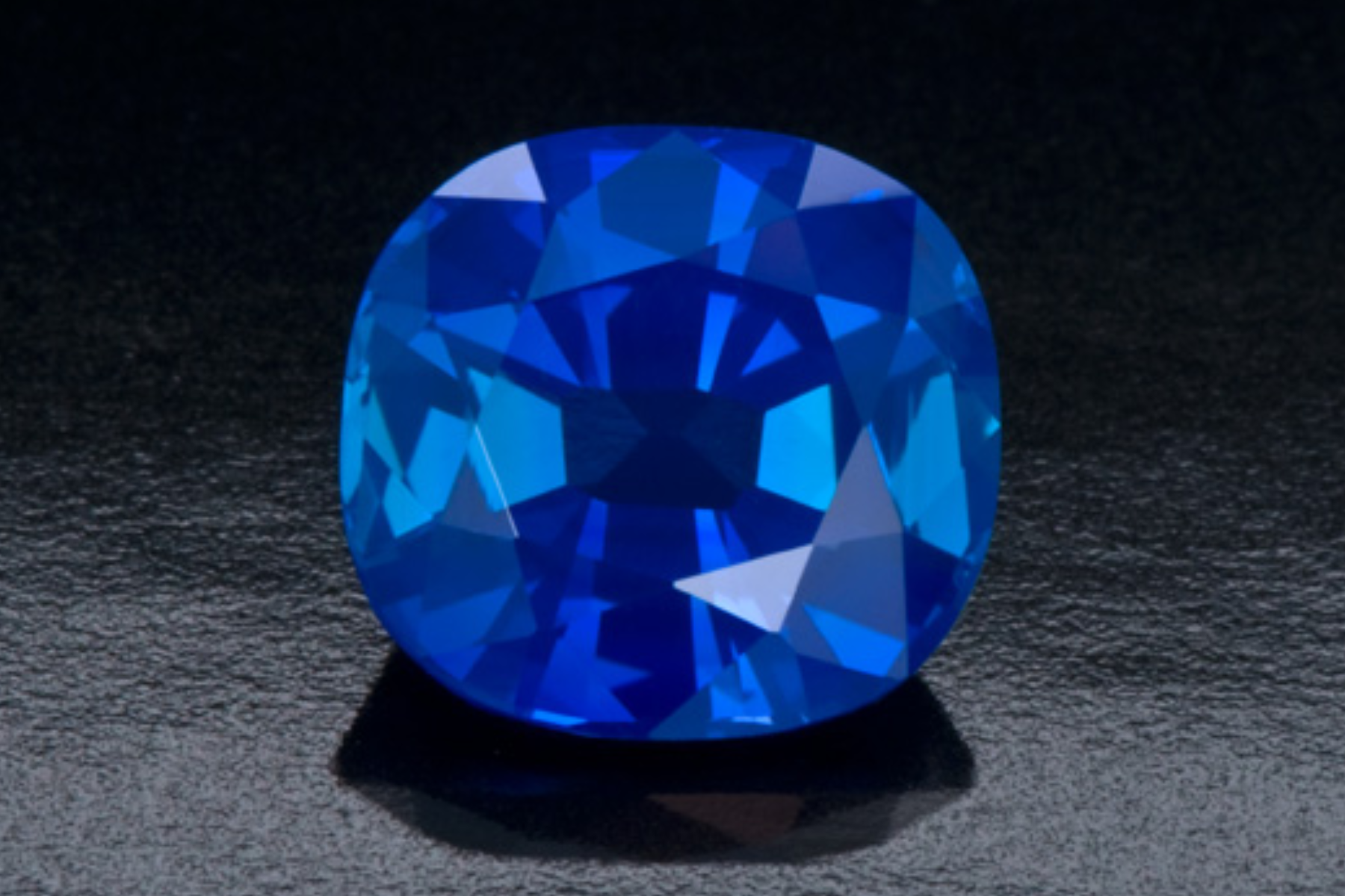 A blue sapphire with rounded edges is displayed on a partially dark background