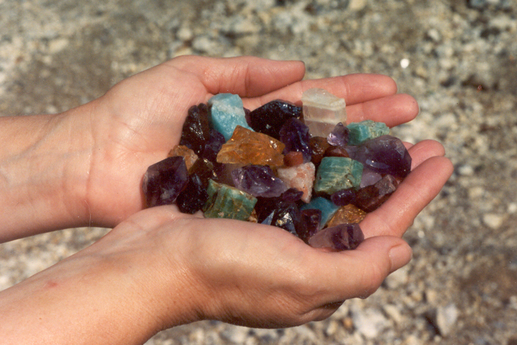 A person's hand holding a large quantity of gemstones on a mining site