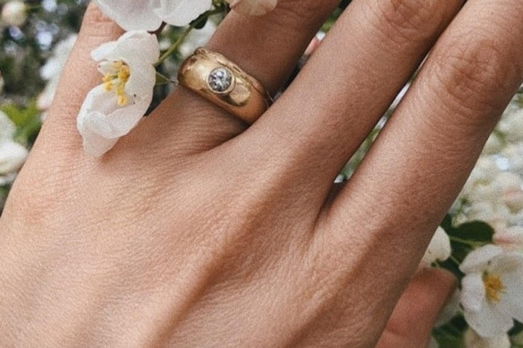 A woman's hand holding a flower while wearing an engagement ring with a flush setting