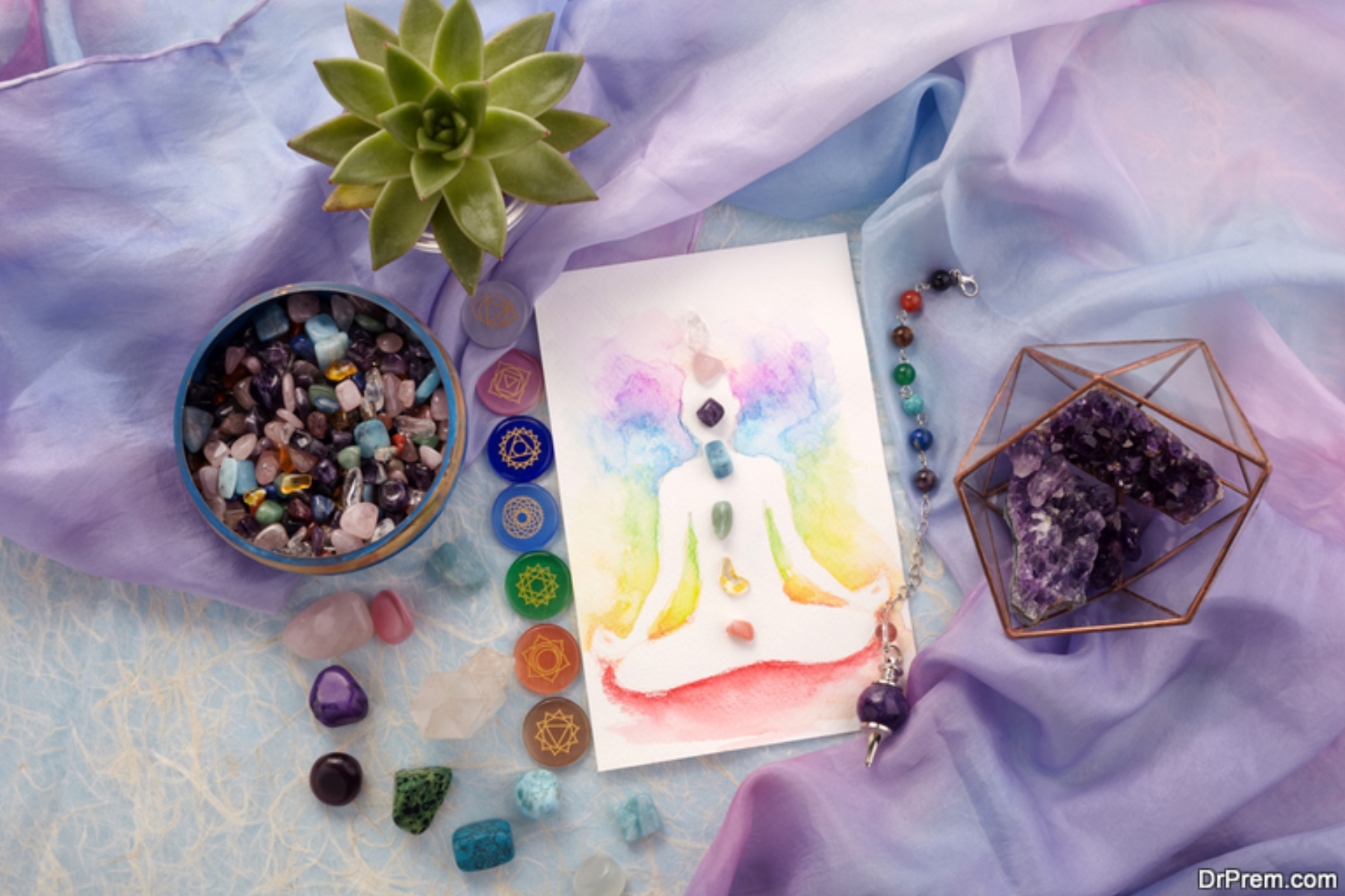 Various gemstones on top of a bedsheet with paper with the art of a meditating person