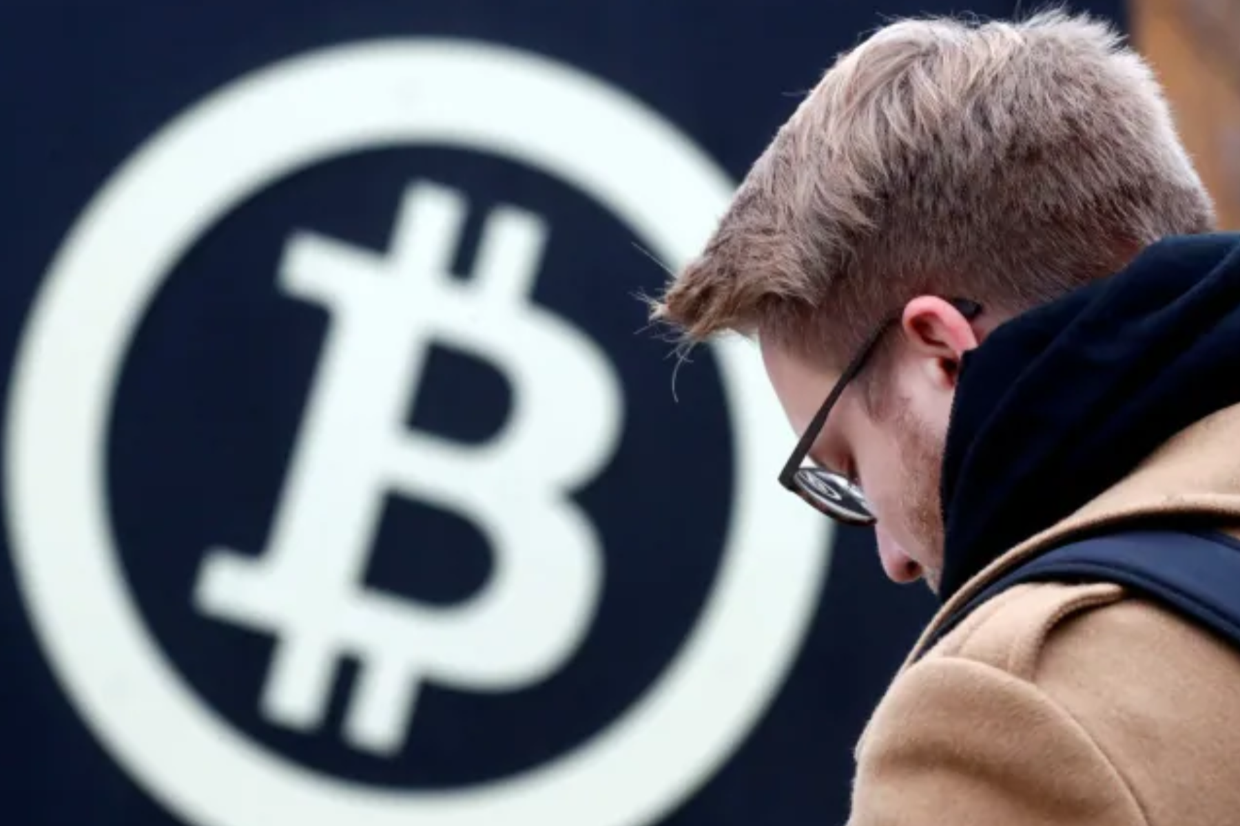A person standing in front of a logo with the word "Bitcoin" written on it