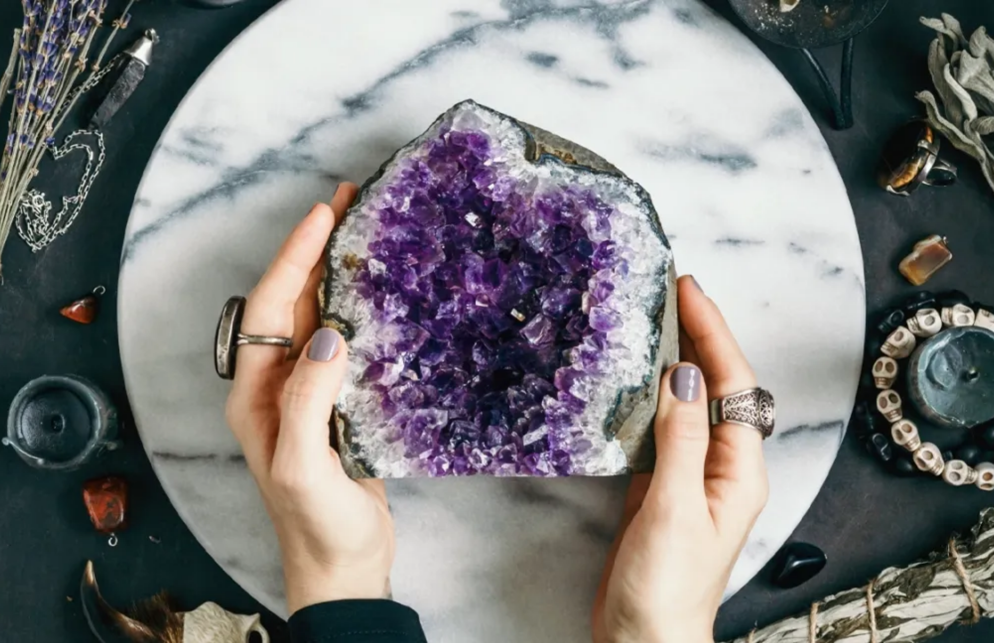 An amethyst stone on a table carried by a woman, as well as several items for healing activities