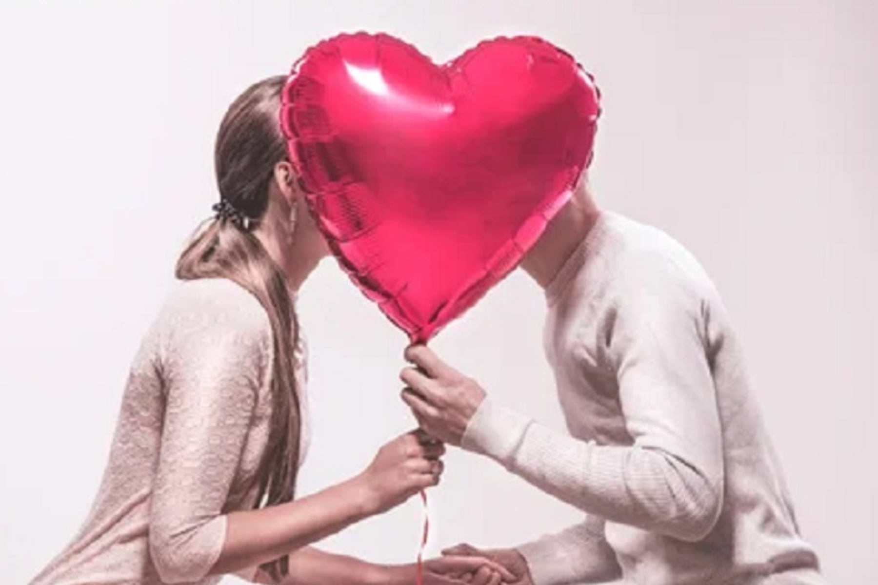 A guy and a woman are kissing behind a Valentine's balloon
