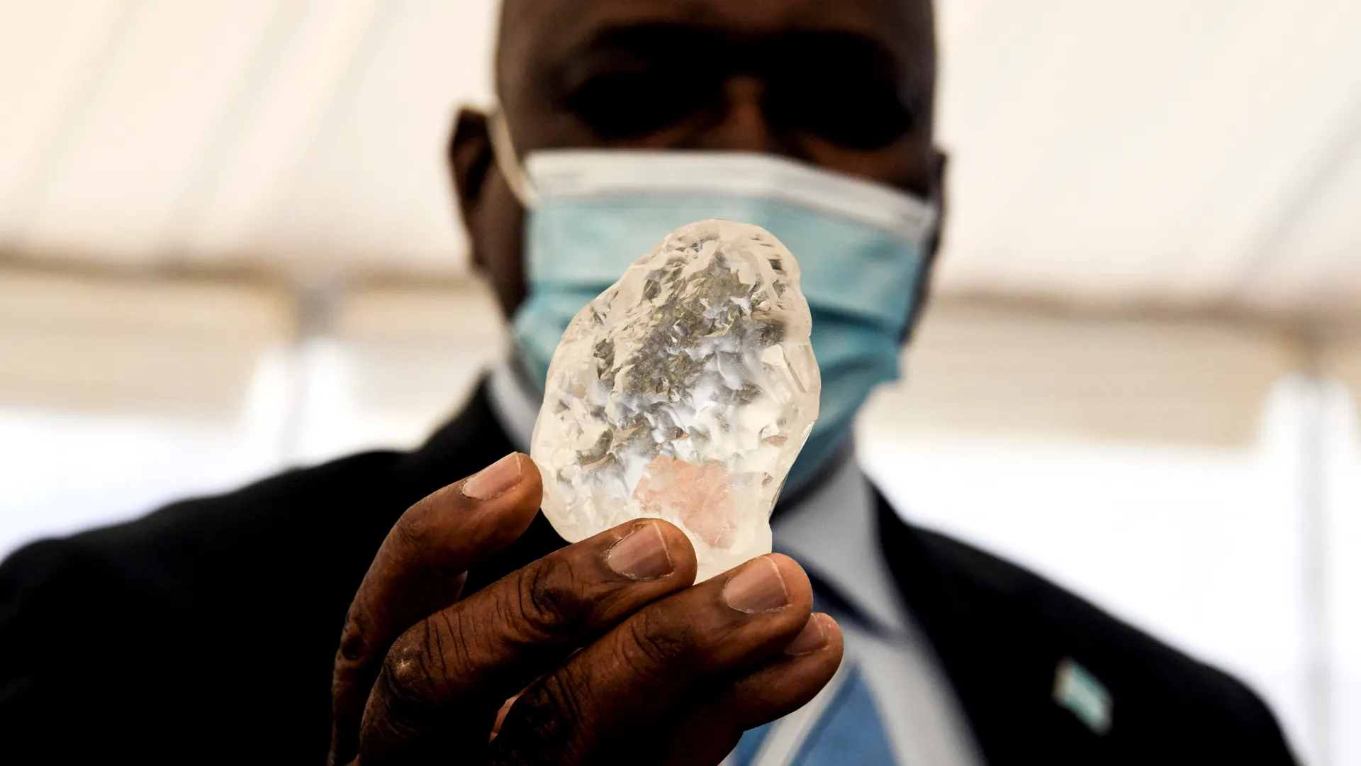 A man wearing face mask is holding diamond in his hand.