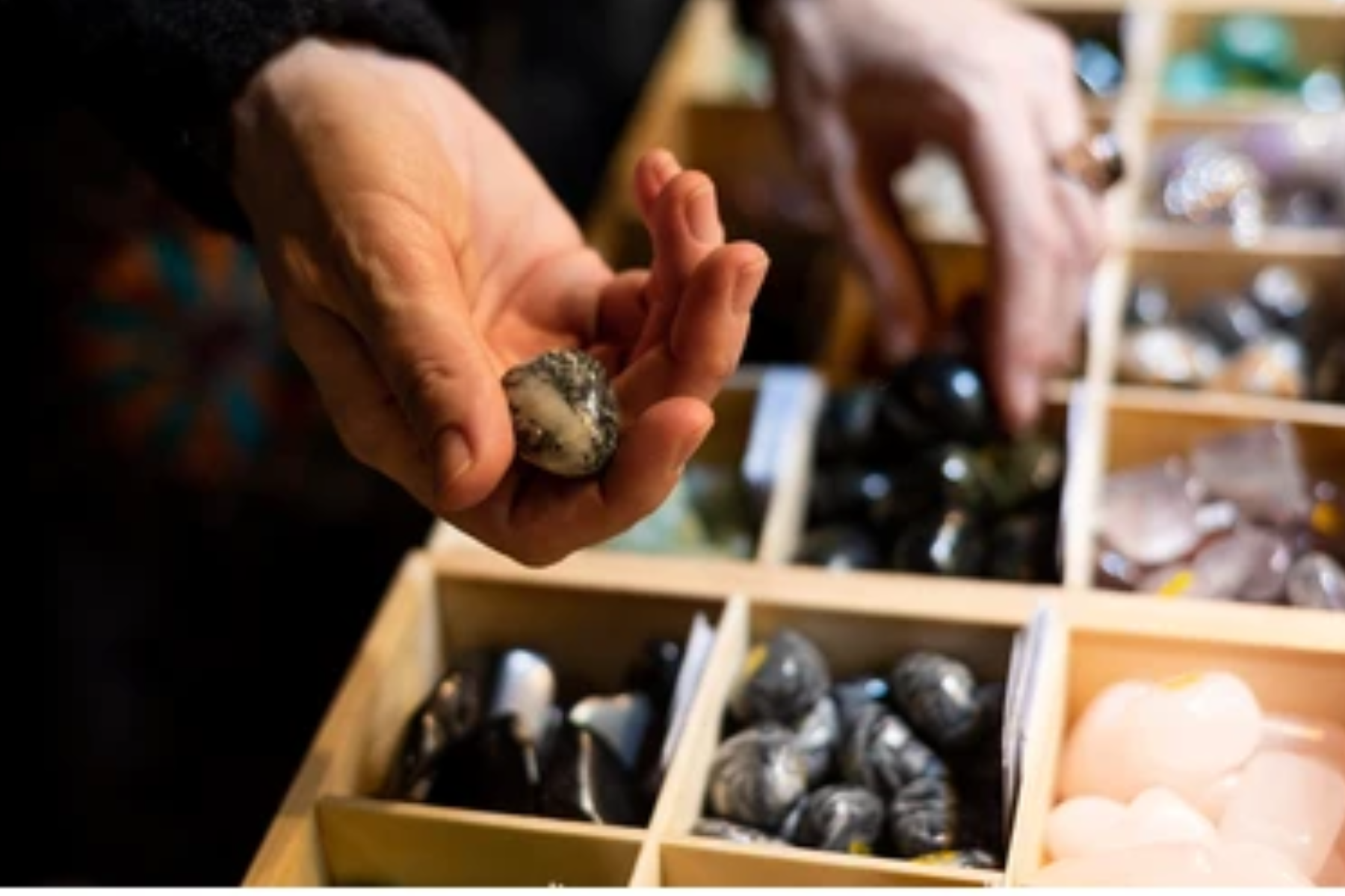 A person's hand selecting a gemstone from the boxes