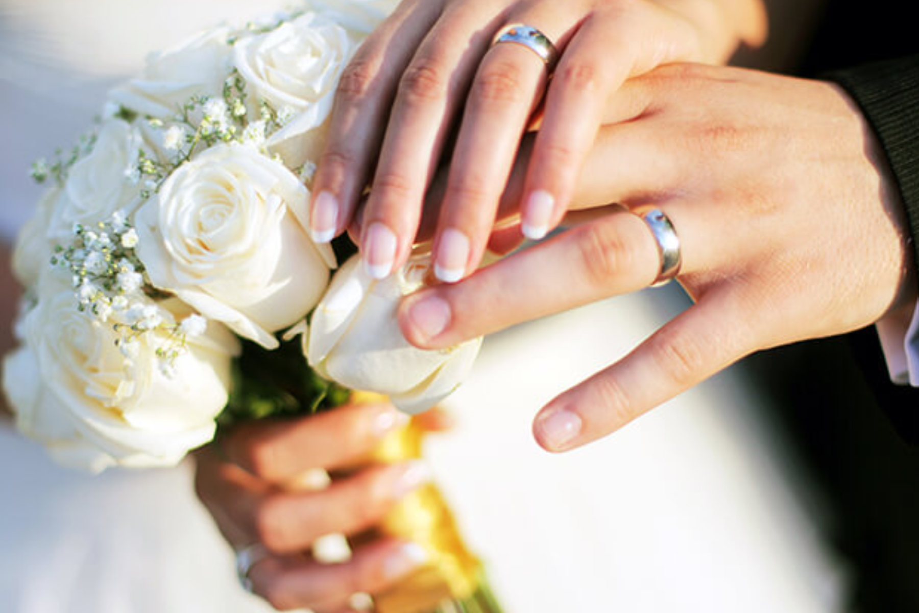 Hands of a wedded couple holding a bouquet and rings