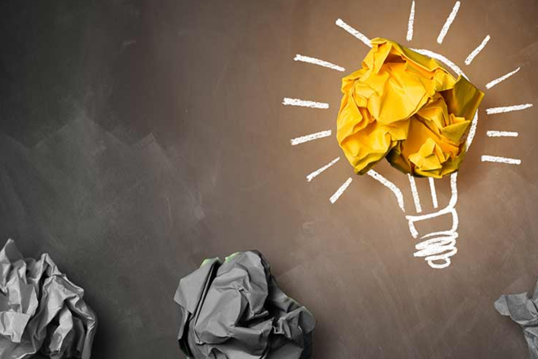 A lightbulb with yellow crumpled paper and three crumpled gray papers