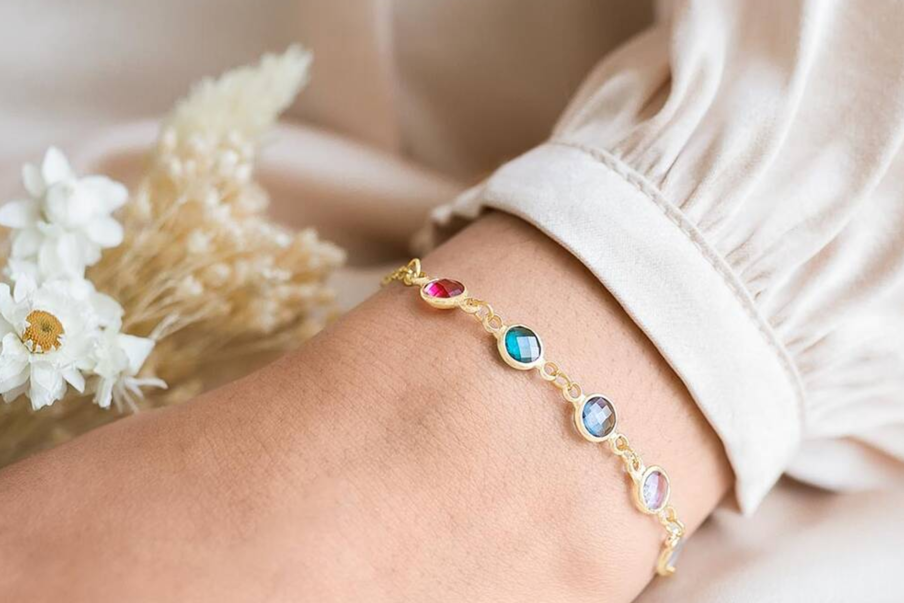A woman's forearm is adorned with bracelets containing various birthstones