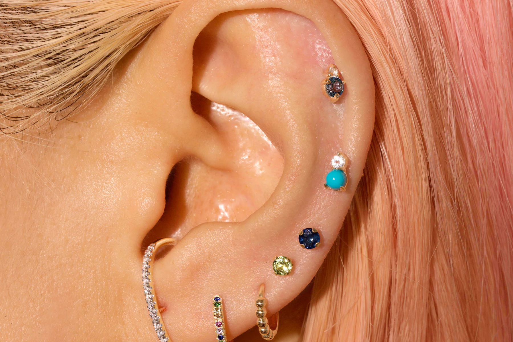 Different varieties of birthstone earrings adorn the ear of a woman