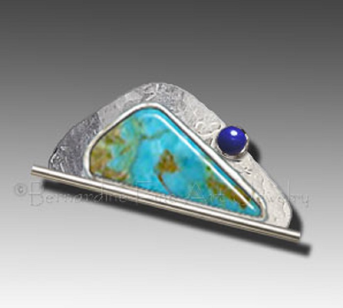 A silver brooch with turquoise both shaped like a scalene triangle with curved edges and a small round lapis lazuli