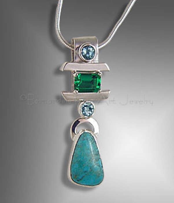 A silver pendant with teardrop-shaped turquoise and a rectangular emerald between two small round topaz